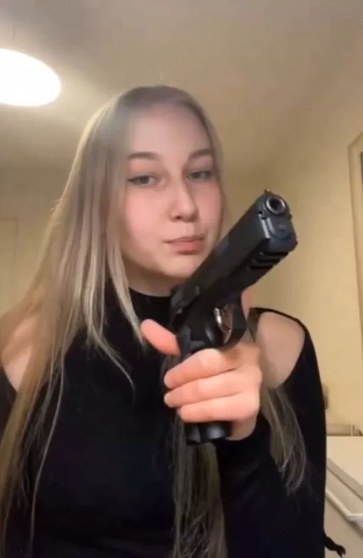 Evita Kolmonen pukeutunut mustaan mekkoon aseen kanssa.